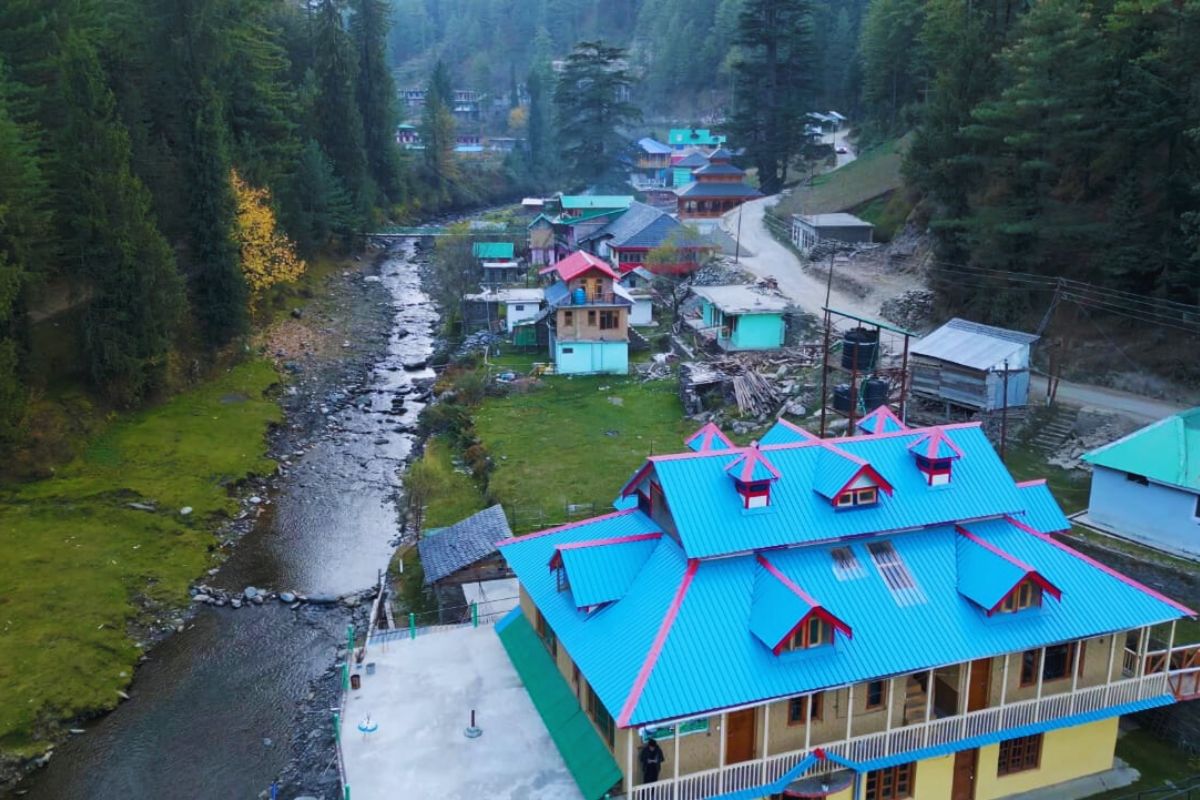Scenic view of Gada Gushaini village with river, pine trees, and traditional wooden homes in Inner Seraj, Himachal Pradesh 