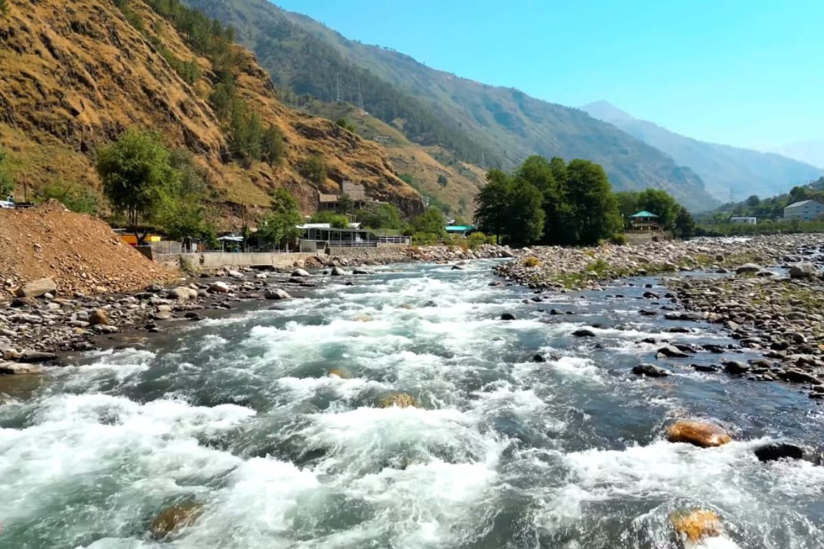 Jibhi village nestled in the Tirthan Valley with wooden cottages, lush pine trees, and a serene mountain stream 