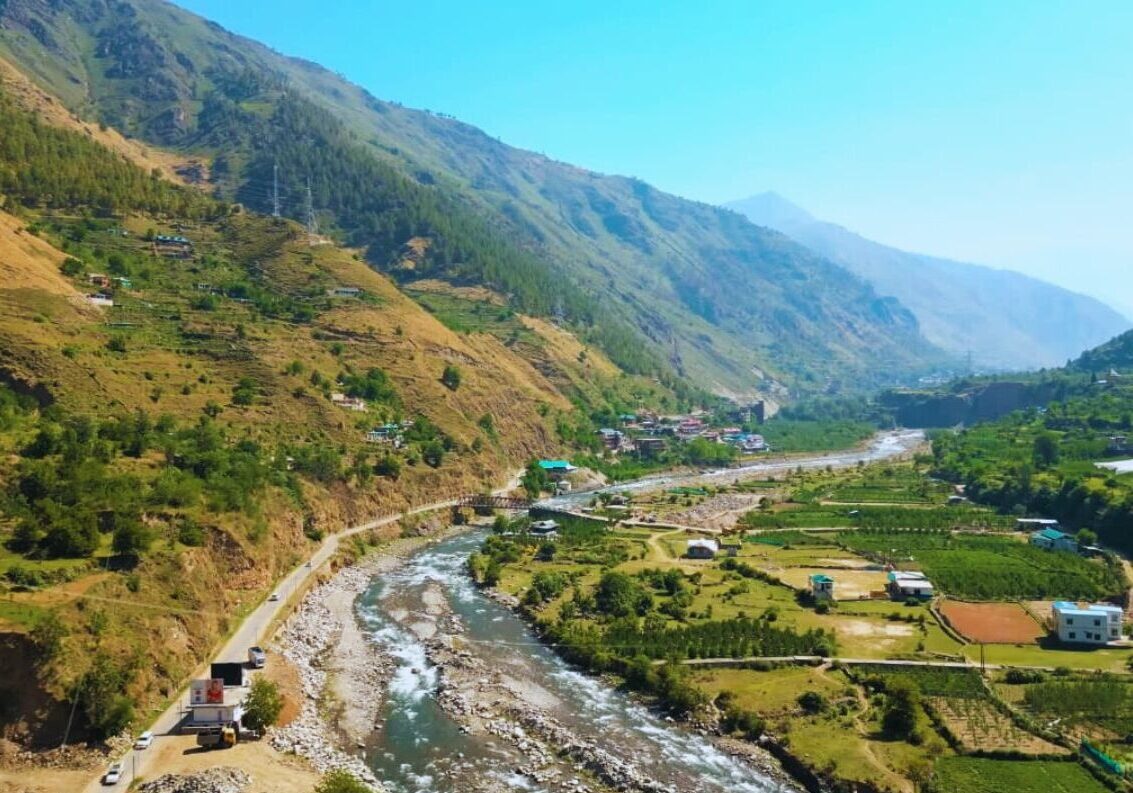 Kalga village in Parvati Valley surrounded by apple orchards and wooden houses with Himalayan mountains in the background 