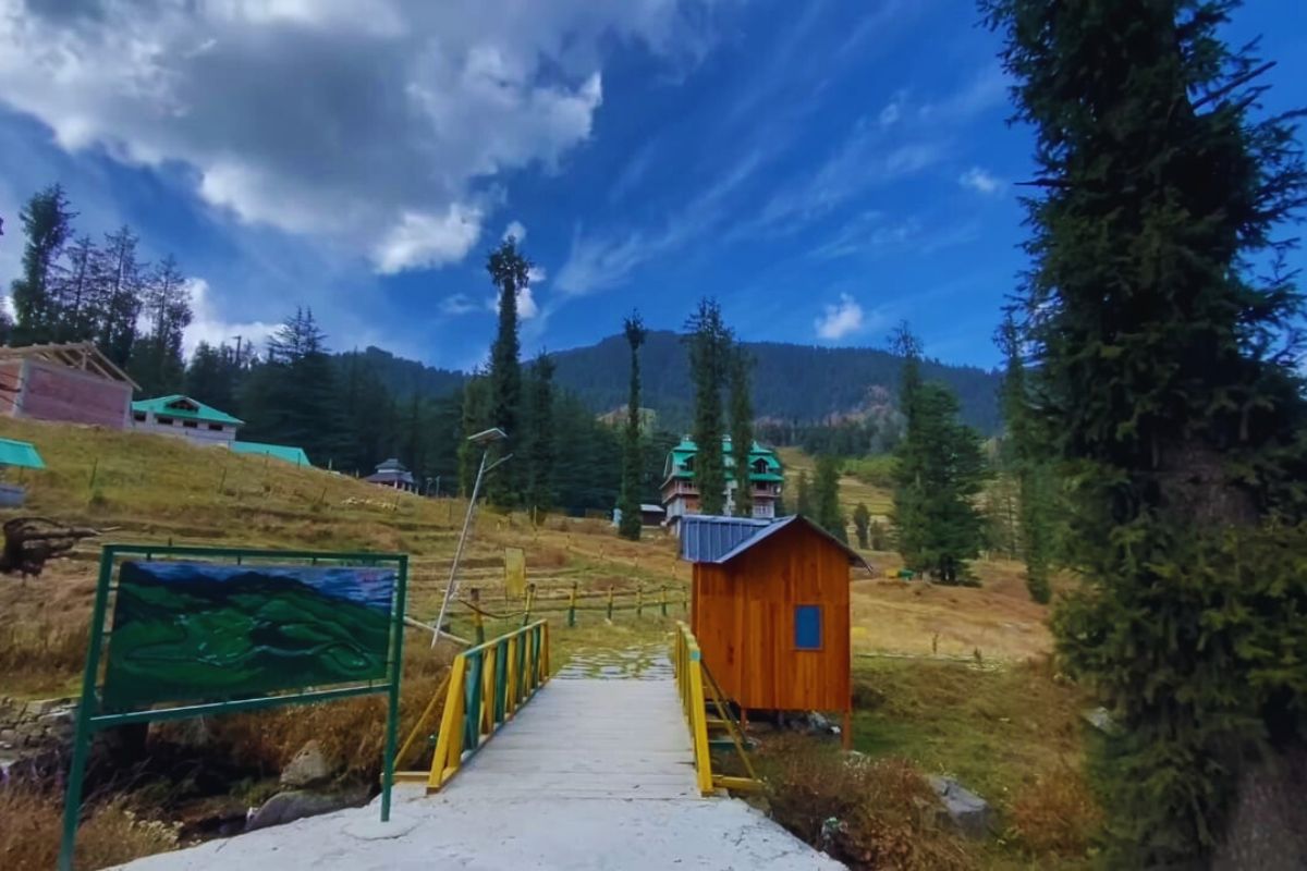 Tirthan River flowing through a forested valley with pine trees and wooden cottages in Himachal Pradesh 