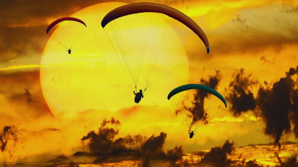Three paragliders flying in front of a dramatic golden sunset sky